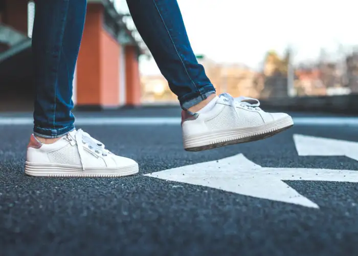 Close up of a person wearing white sneakers crossing the street